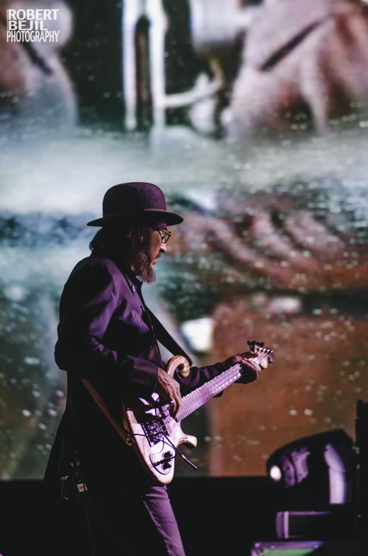 a man holding a guitar on stage in front of a large screen