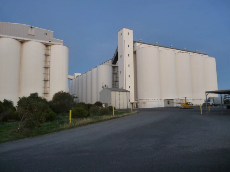 a street is shown with parked cars near two large silos