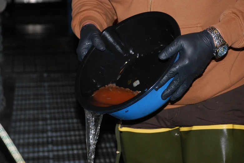 someone wearing gloves and holding a bowl that has liquid in it