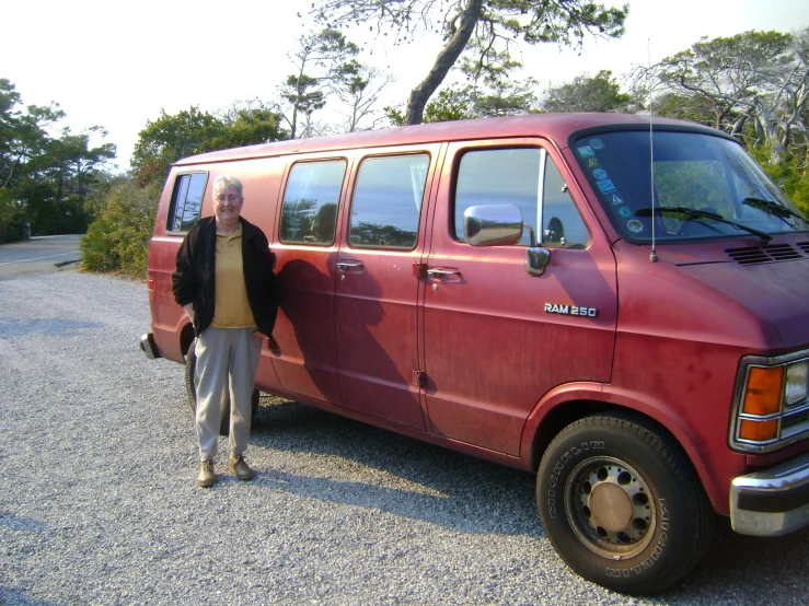 a man in black jacket and sunglasses standing by an older purple van