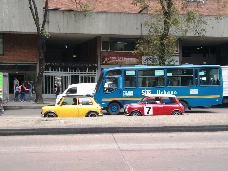 two small cars sitting in front of a blue and white bus