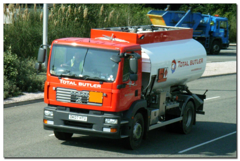 a bright orange truck carrying a fuel tanker on a street