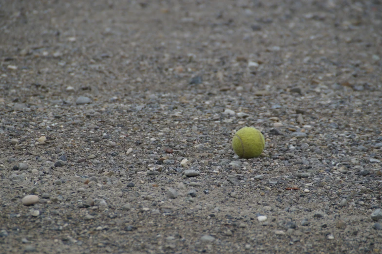 an unidentifiable looking tennis ball sits on some gravel