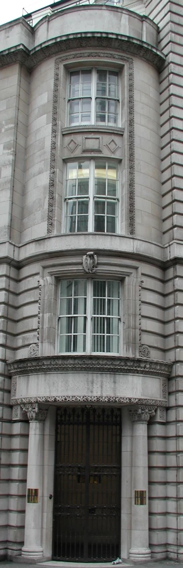 a clock in a tall grey brick building with two story windows