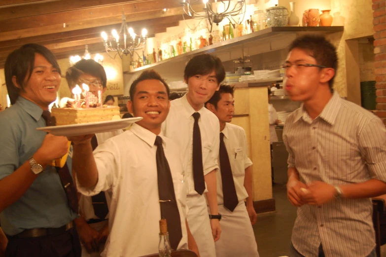 some asian men standing together and holding a plate of cake