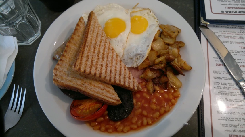 a plate of eggs, beans and toast with tomato on the side