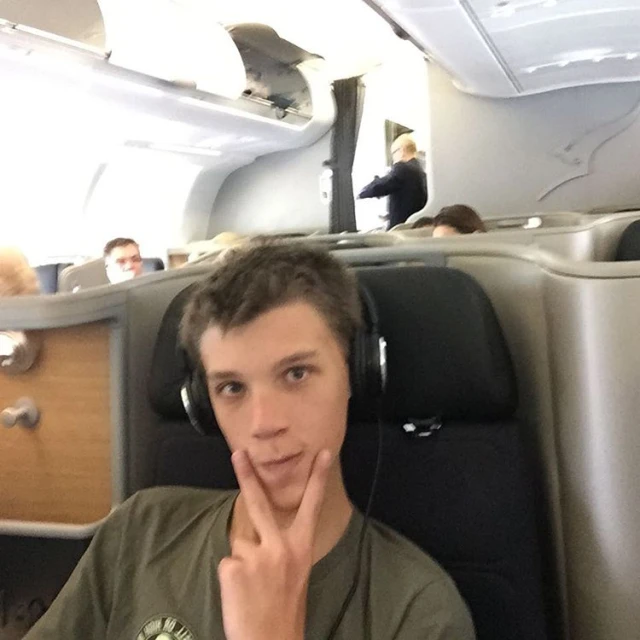 a man with headphones sitting on an airplane with his hand near his face