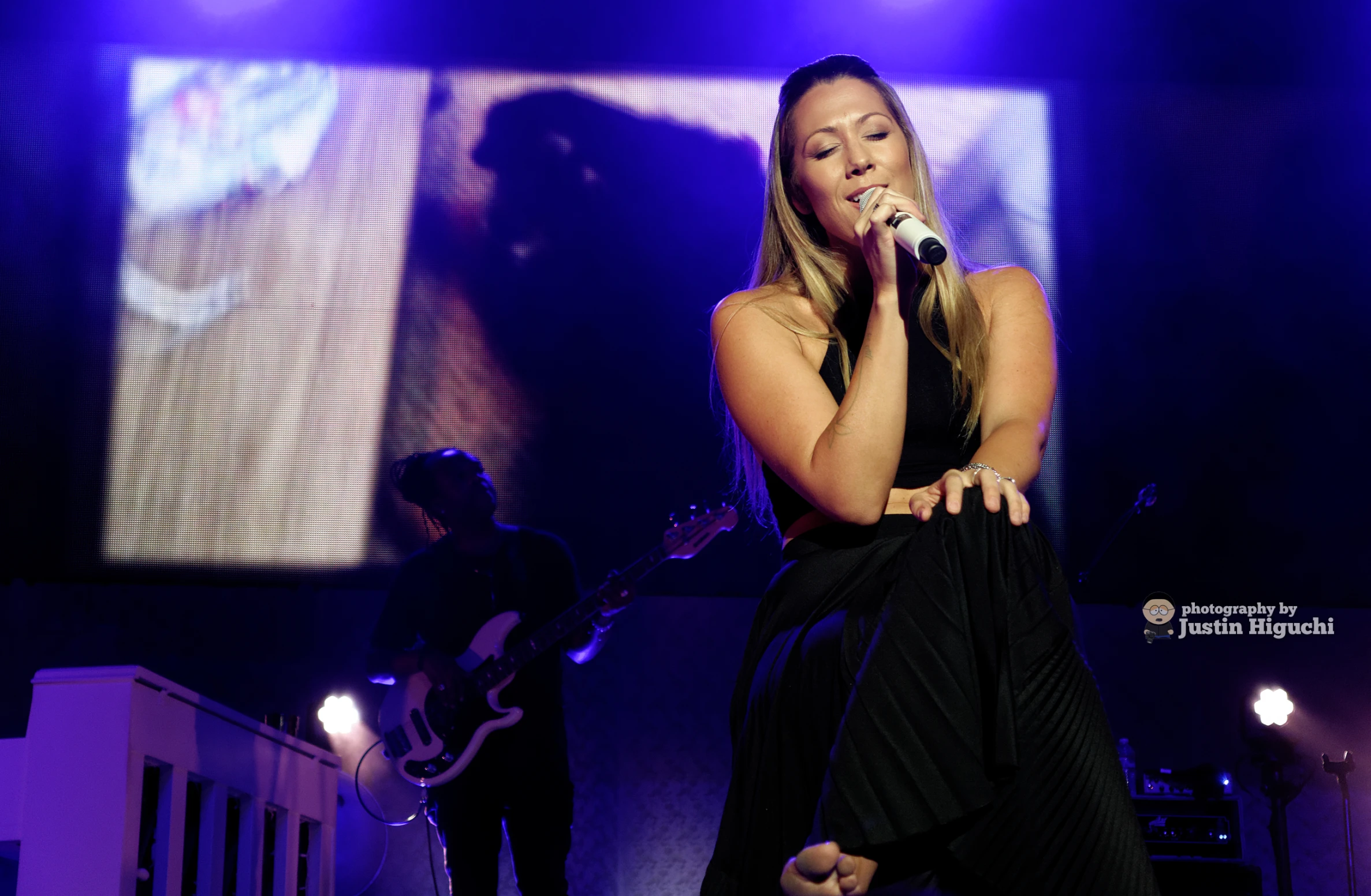 a woman wearing a black dress on stage with purple lights and a guitar