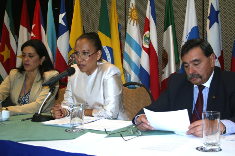 four people sitting at a conference table in front of flags