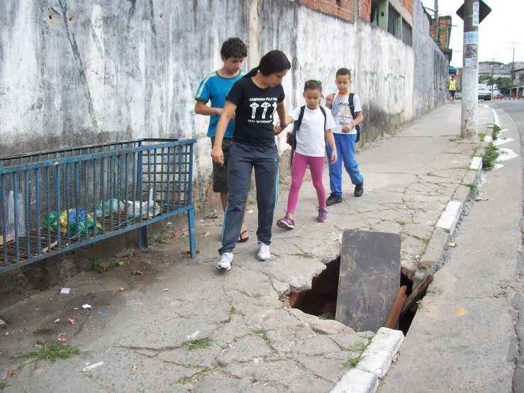 children walking on sidewalk next to cement pipe