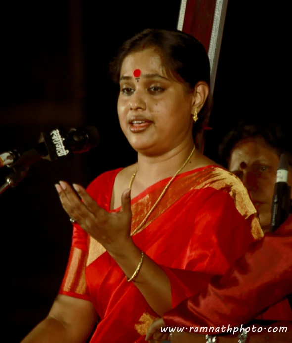 an indian woman in red sari speaking into a microphone