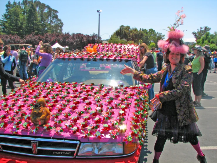 two women in costume standing next to a car covered in flowers