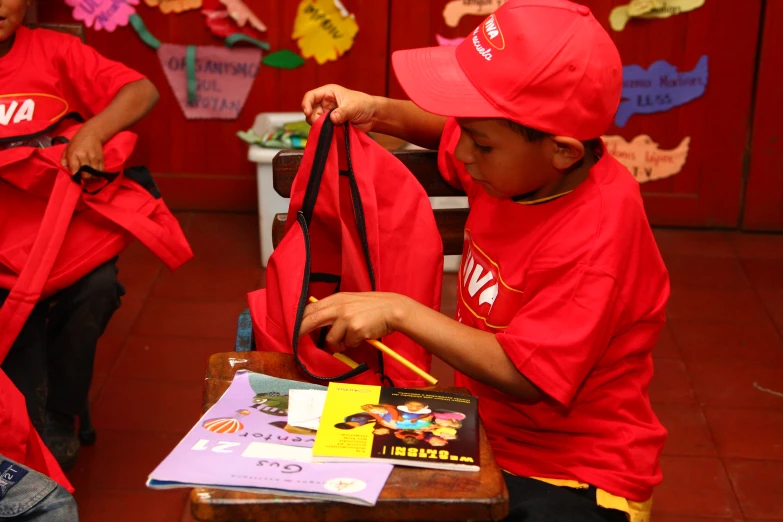 two s wearing red shirts and a hat doing craft