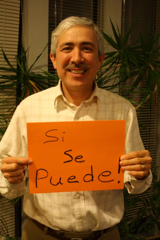 an older gentleman holding a orange sign with the words si se puede