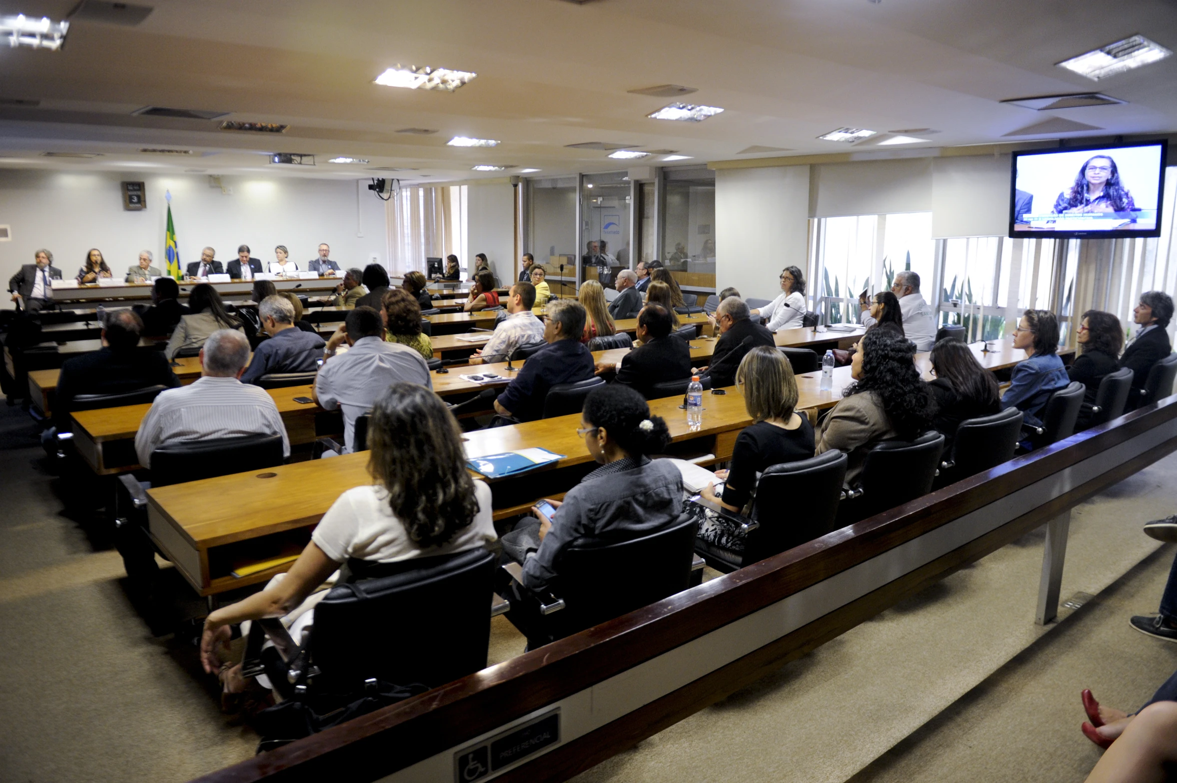 a class room full of people seated in chairs watching television