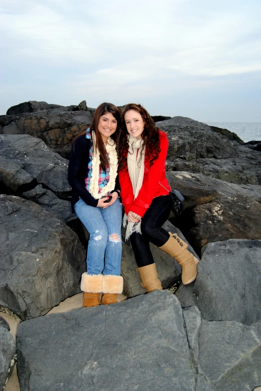 two women sit on the rocks near the ocean