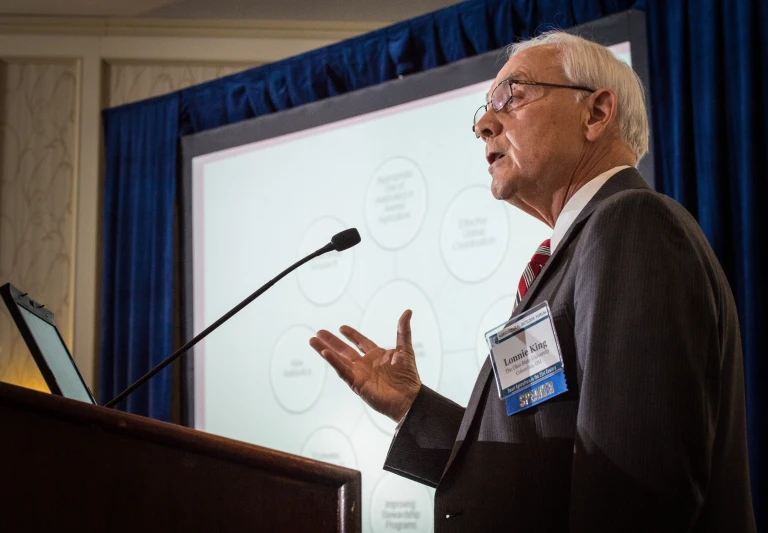 an older gentleman at a podium speaking at an event