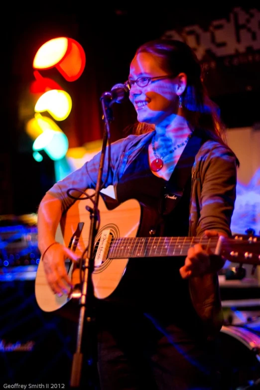 a woman that is playing a guitar in front of a microphone