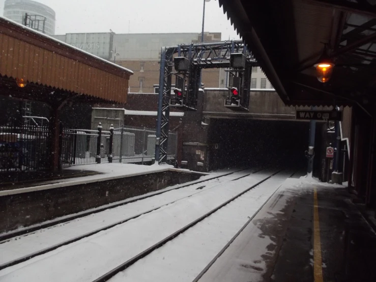 railroad tracks with lights in snowy weather with buildings