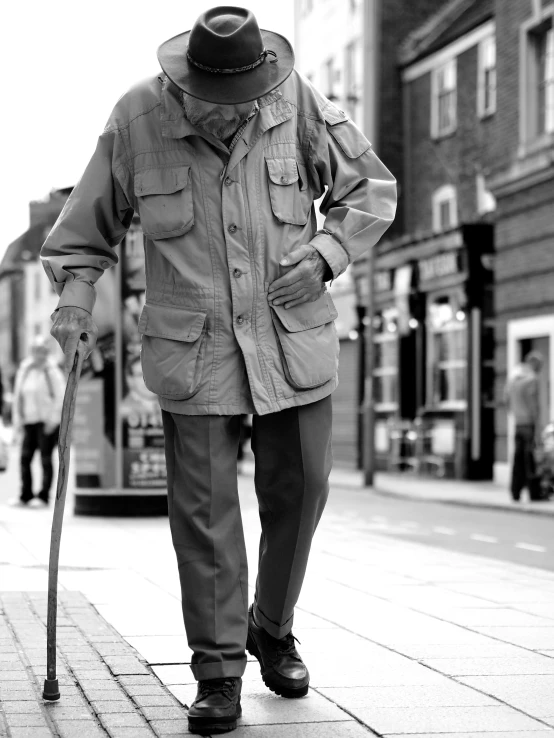 a man with a hat and an old cane walking down a sidewalk