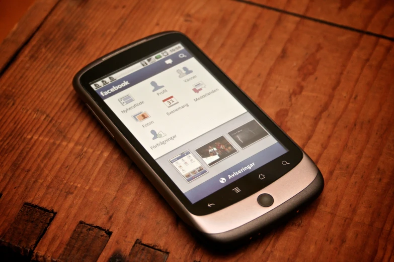 a cellphone sits on a wooden table with an image of facebook