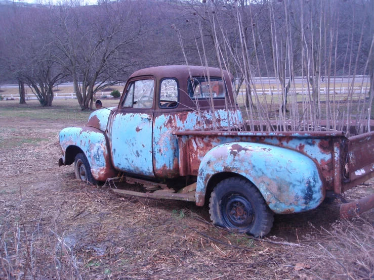 an old rusted, blue truck parked in the woods