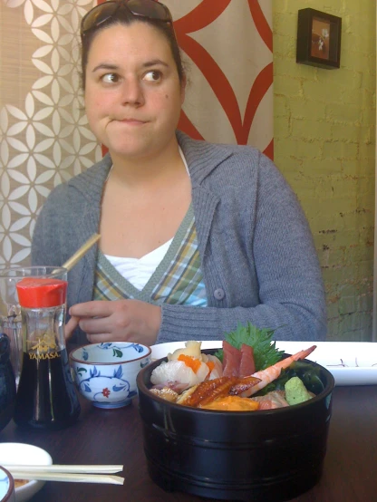 woman sitting at table holding chopstick with sushi in bowl
