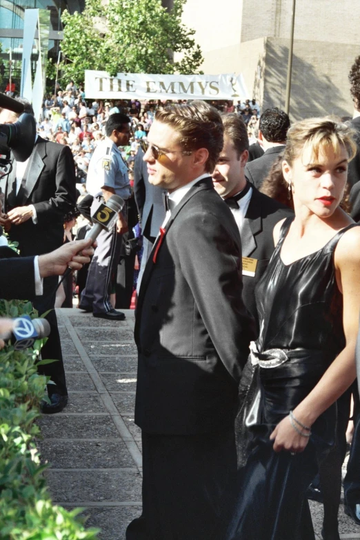 a man in black dress with his hands in his pocket while two women are walking past