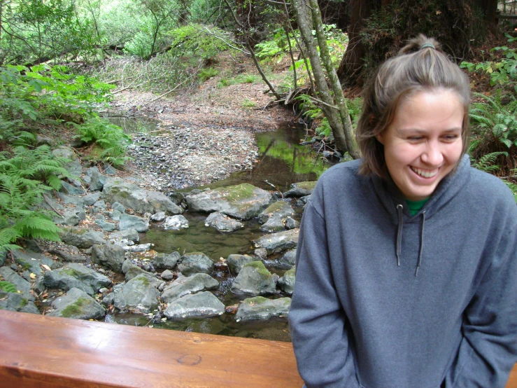 a woman standing in front of a wooden bench near rocks