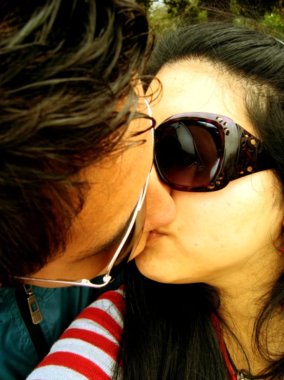 a man and woman kissing each other while wearing sunglasses