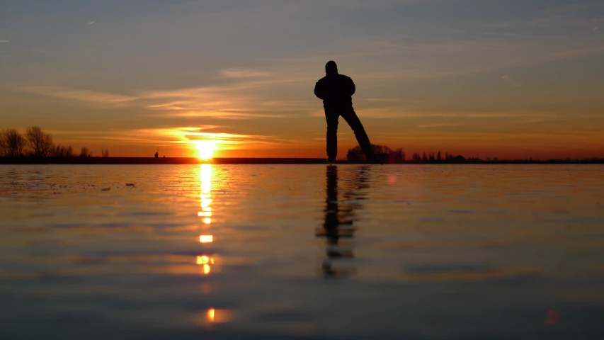 silhouette of man standing with head against body of water during sunset