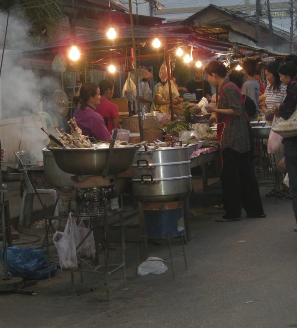 people standing and sitting around a market with some food on top