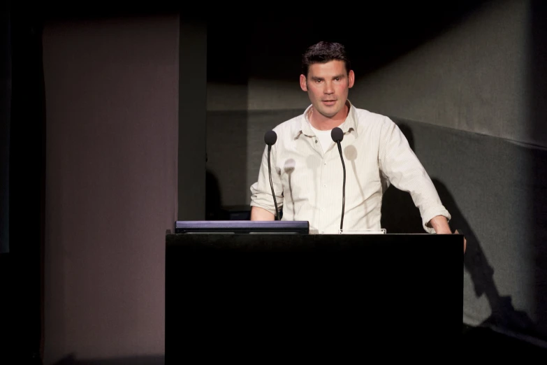 a male in a white shirt and black tie a speaker and a microphone