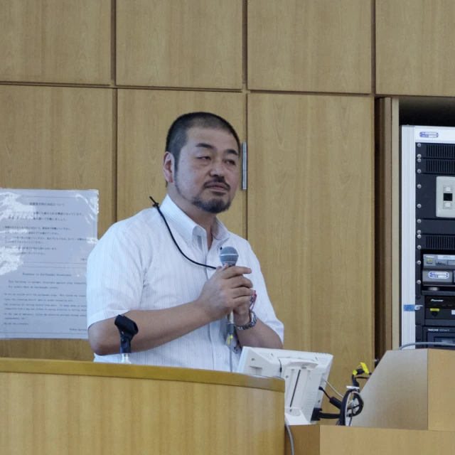 man with microphone standing behind a wooden podium