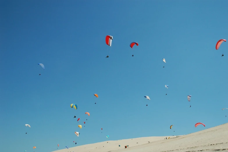 dozens of people who are flying kites on a sand dune