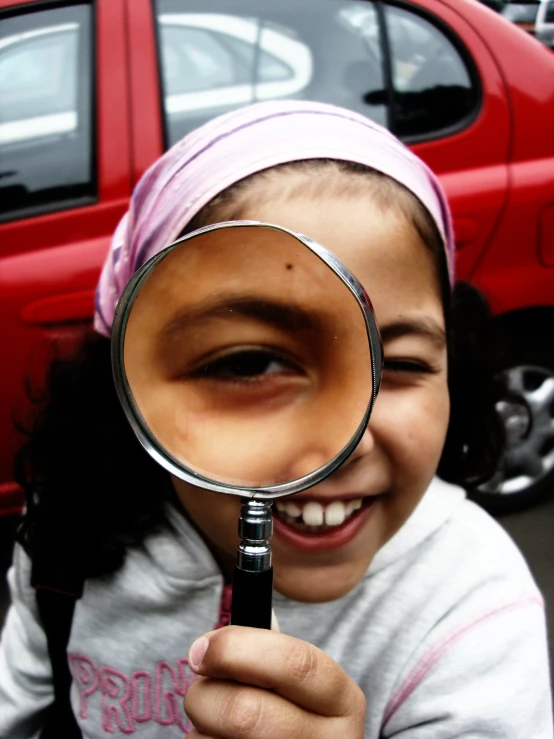 a little girl wearing a bandana holding a magnifying glass