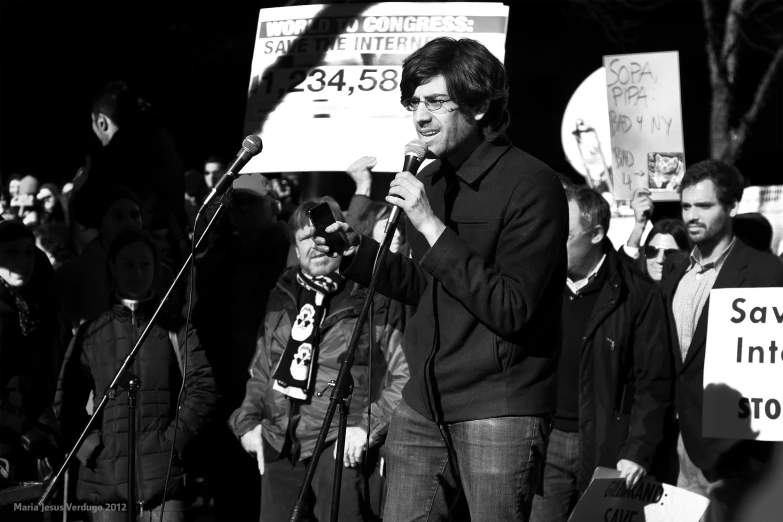 a man standing at a microphone with protest signs in front of him