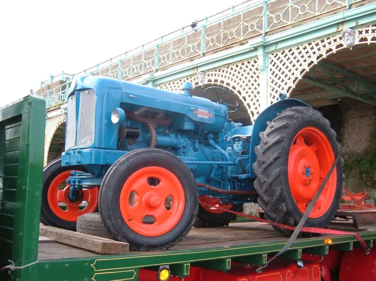 an old blue tractor sitting on top of a semi truck