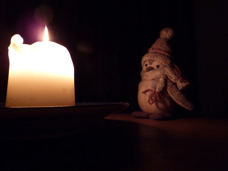 a snowman on a wooden table in front of a lit candle