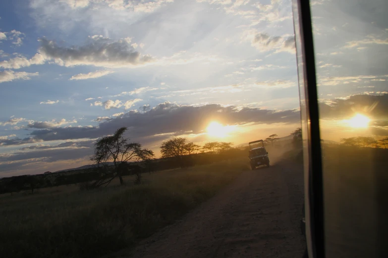 two trucks traveling down the dirt road during sunset