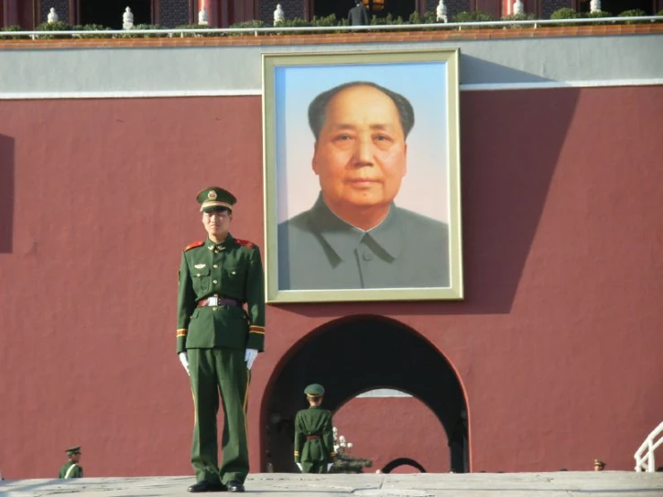a man in uniform and hat standing next to a picture of mao
