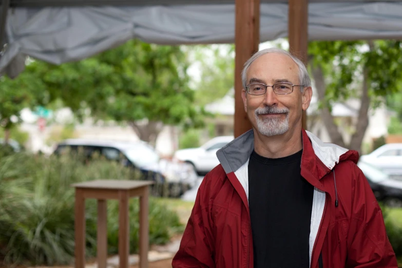 a man with a red coat smiles while under an umbrella