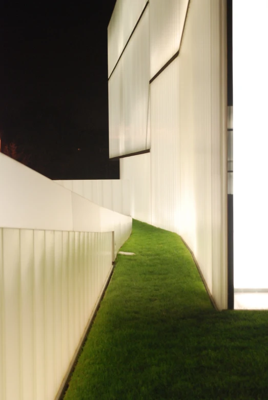 a wall between two tall white buildings with grass on the side of it