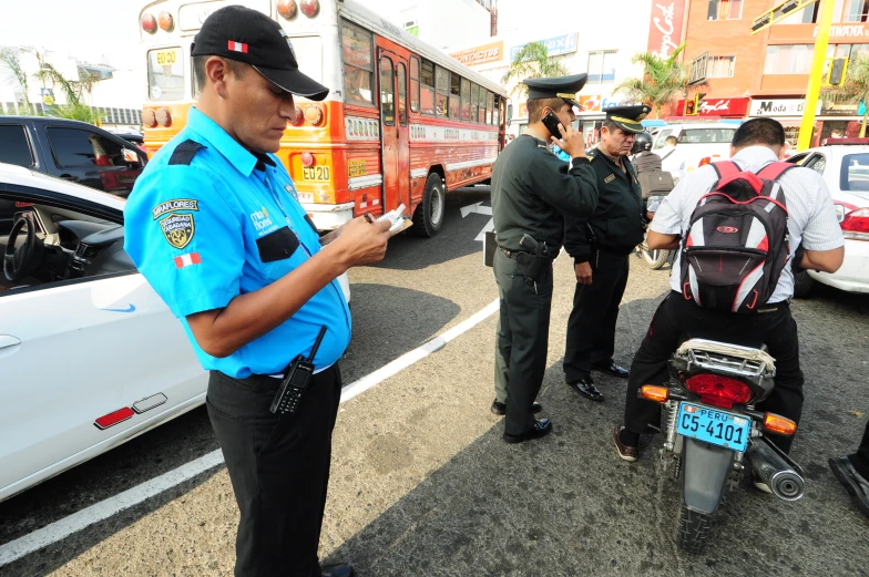 a police officer looking at his phone as two men stand nearby