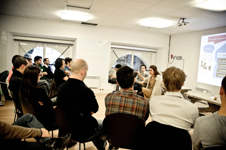 people sitting in chairs facing a screen, watching