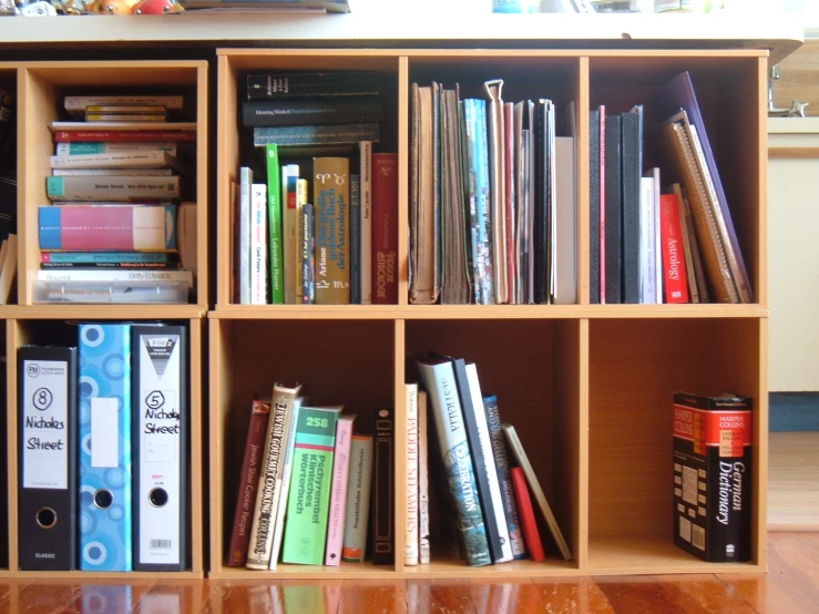 a bookcase filled with books and binders sitting on top of a hard wood floor