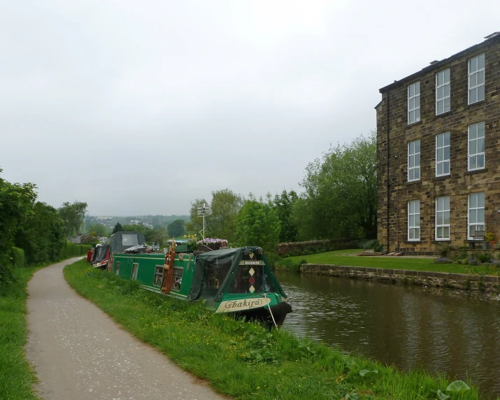 a narrow canal with a green boat docked next to it