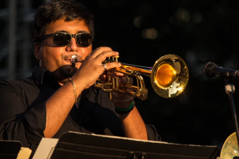 man wearing sunglasses and playing a trumpet in front of a crowd