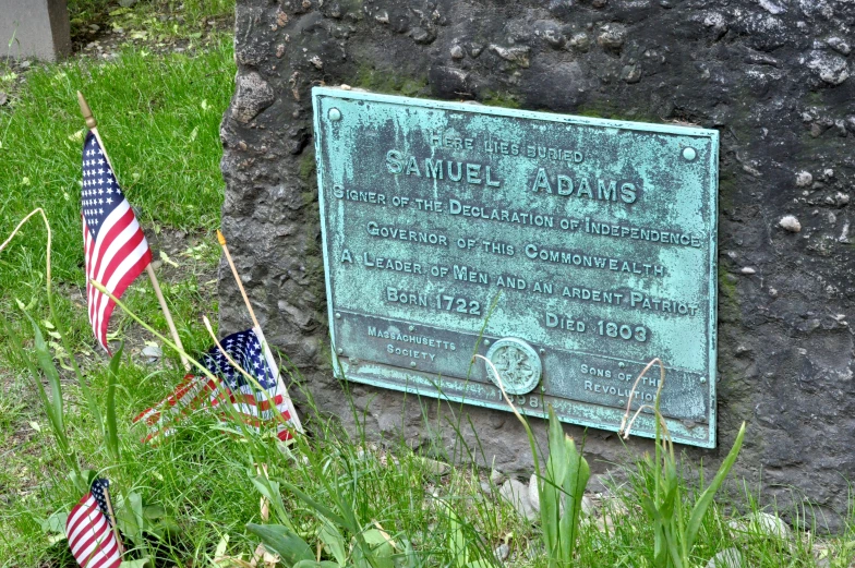 an old plaque on grass that has two flags