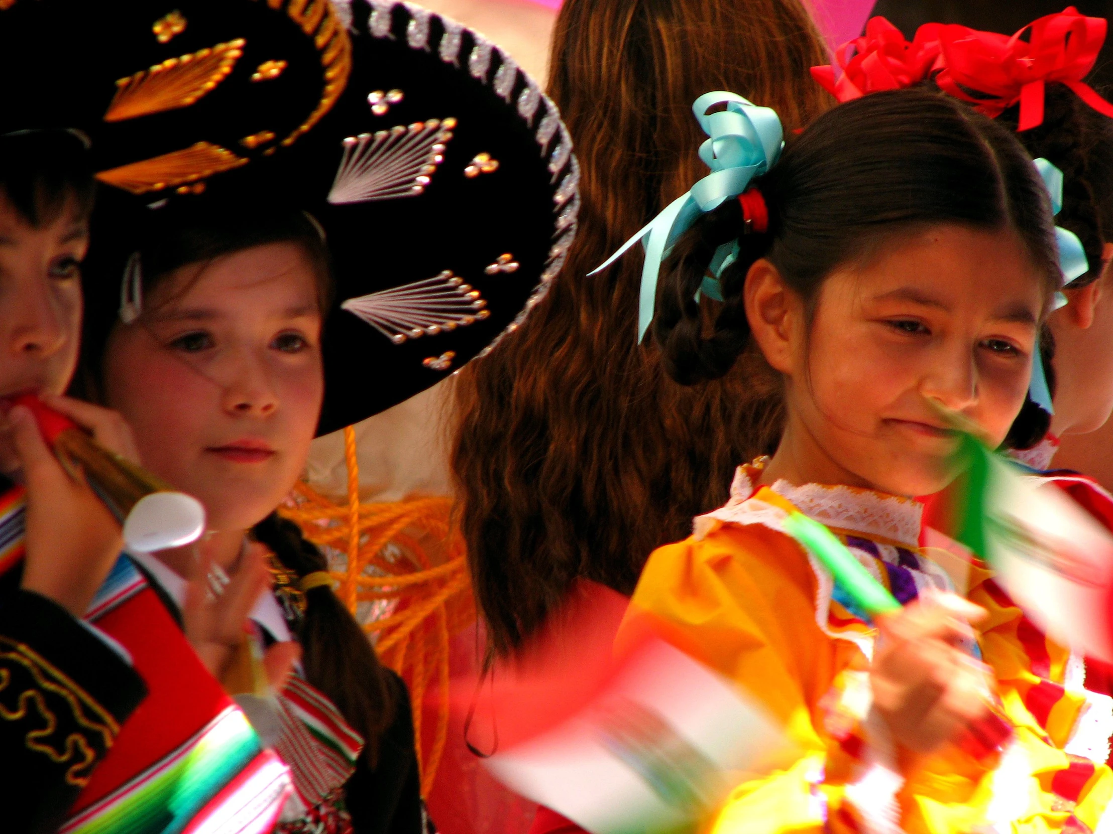 two girls dressed in costume hold flags, one girl with dark hair and one wearing bright clothing